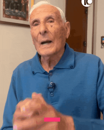 an elderly man wearing a blue shirt with a microphone on his collar