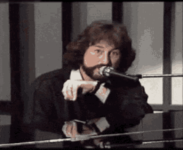 a man with a beard is singing into a microphone while standing at a piano .