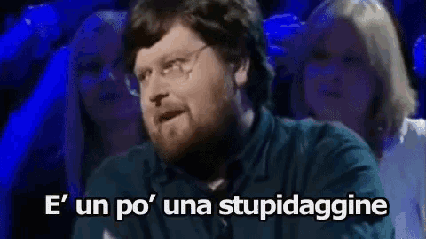 a man with glasses and a beard says e ' un po ' una stupidaggine in front of a crowd of people