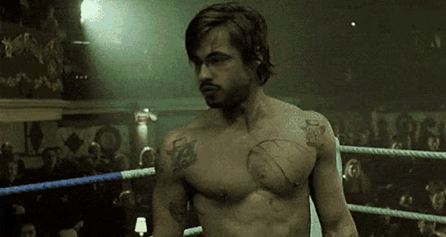 a shirtless man is standing in a boxing ring with a crowd watching .
