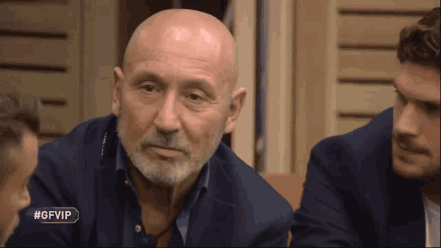 a bald man with a beard is sitting in front of a sign that says #gfvip on it