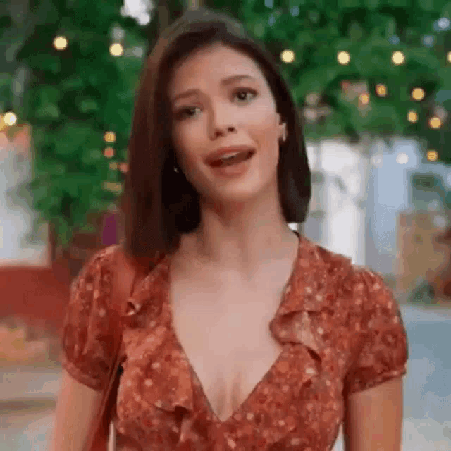 a woman in a red dress with a plunging neckline is standing in front of a tree .