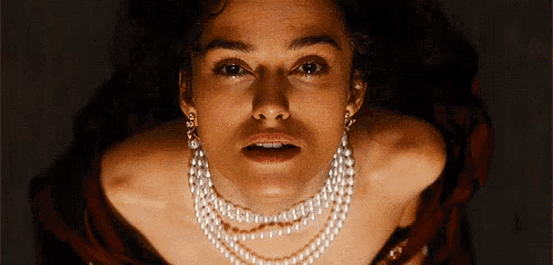 a woman wearing a pearl necklace and earrings is looking up at the camera .