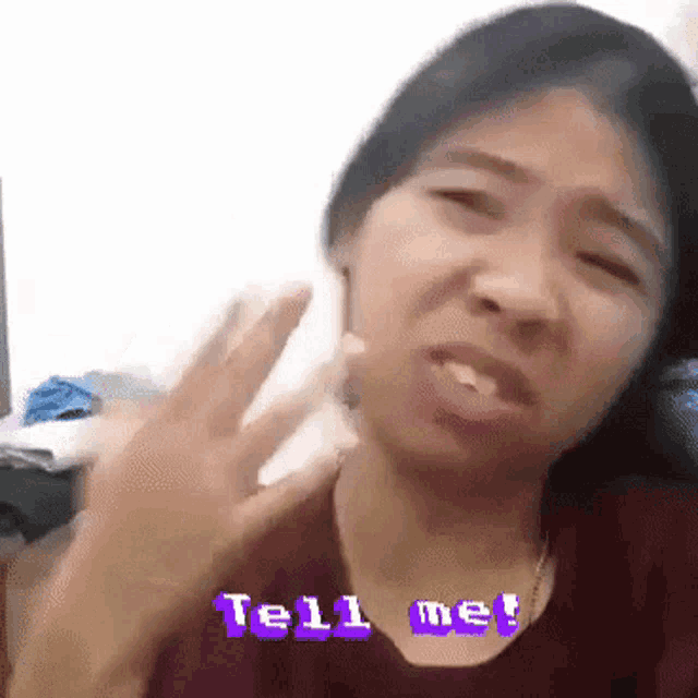 a woman is making a funny face with the words tell me behind her