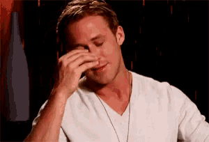 a man in a white shirt wipes his face with his hand