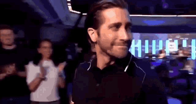 a man in a black shirt is smiling in front of a crowd of people