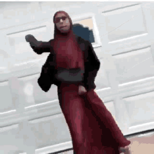 a woman in a red dress and sunglasses is dancing in front of a garage door