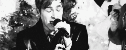 a man is singing into a microphone with his eyes closed in a black and white photo .