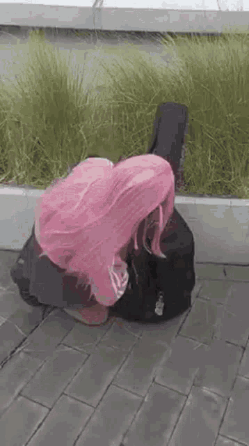 a woman with pink hair is kneeling down on the ground next to a guitar case .