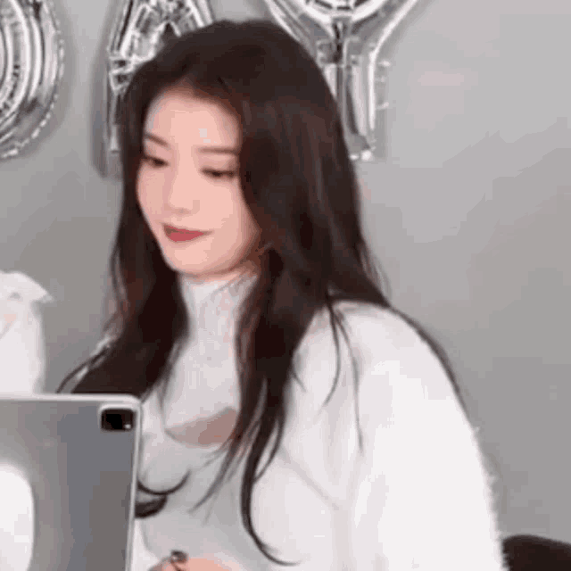 a woman in a white sweater is sitting in front of a laptop .