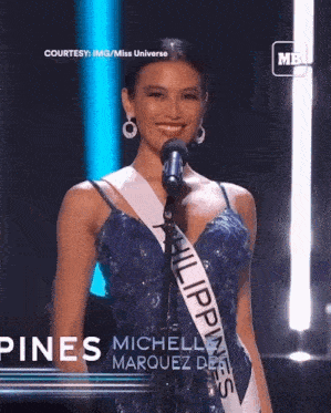 a woman in a blue dress with a sash that says philippines on it stands in front of a microphone