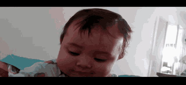 a baby with a blue shirt on looks at the camera with a serious look on his face