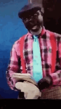 a man wearing a plaid shirt and suspenders is holding a hat .