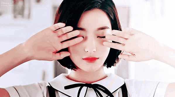 a woman is covering her eyes with her hands and looking at the camera .