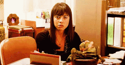 a woman is sitting at a desk in a room with a plant in a pot .
