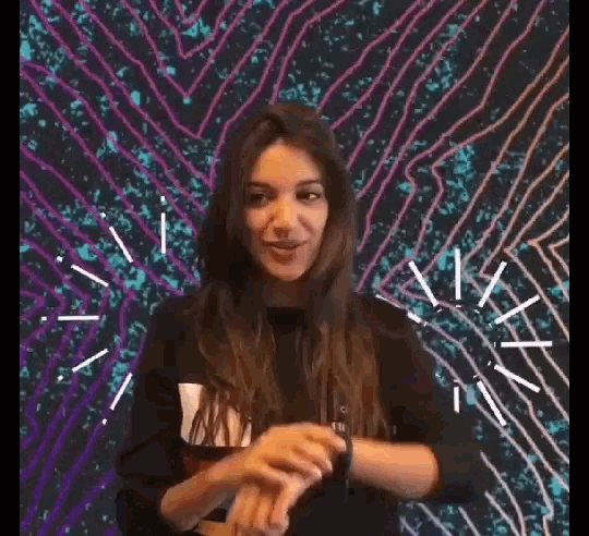 a woman is laughing in front of a colorful background while a person holds her hand .