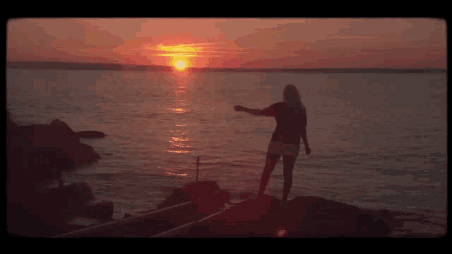 a woman stands on a rock in front of the ocean at sunset