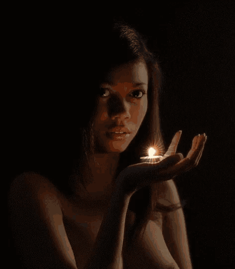 a woman is holding a lit candle in her hand in the dark