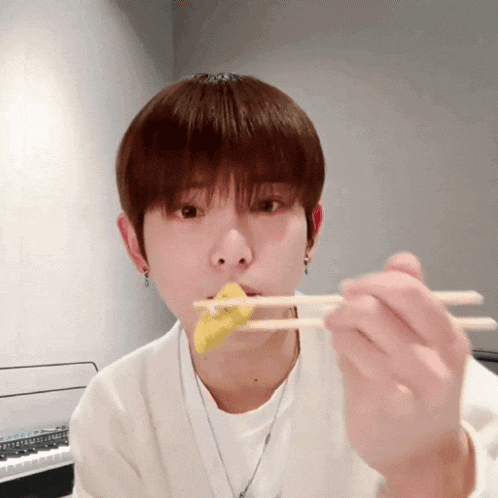 a young man is eating something with chopsticks while looking at the camera