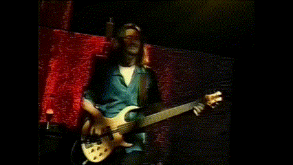 a man with long hair playing a guitar in front of a red curtain