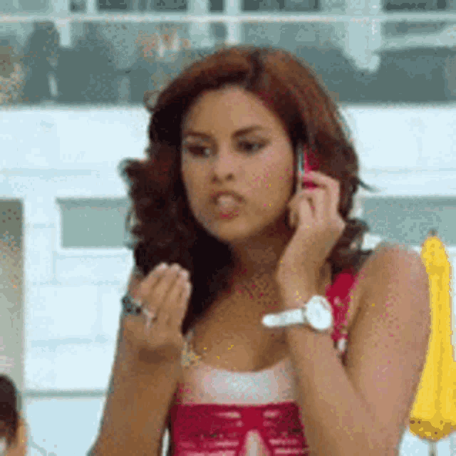 a woman in a red tank top is talking on a cell phone