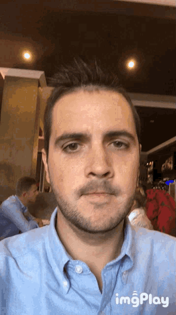 a man in a blue shirt is taking a selfie with imgplay written below him