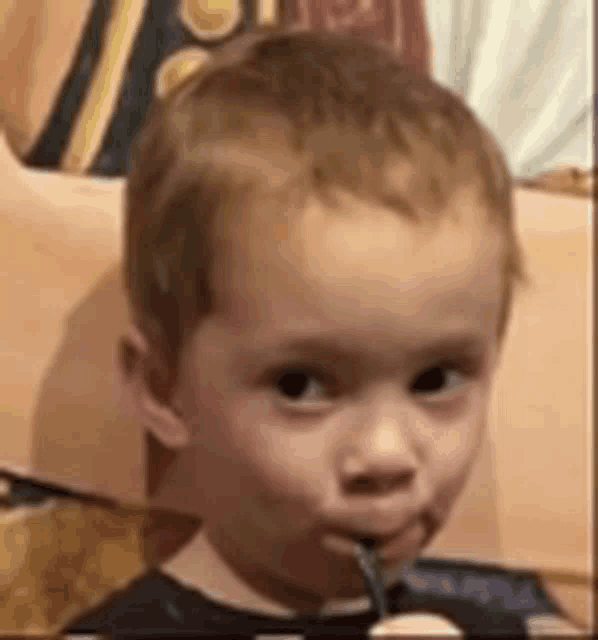 a young boy is holding a fork in his mouth and looking at the camera .