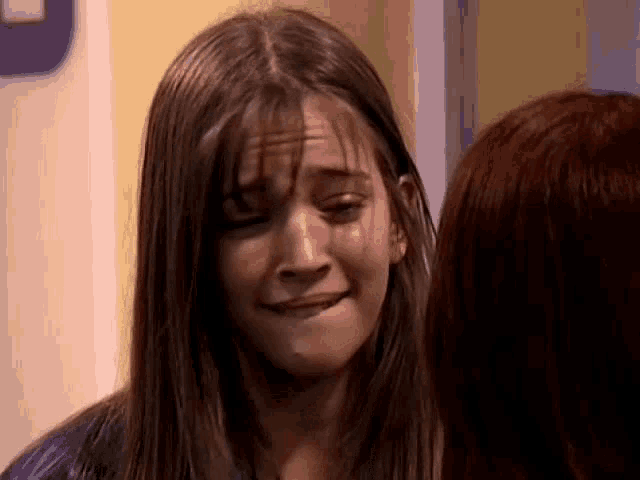 a young girl is crying and making a funny face while standing next to another girl .