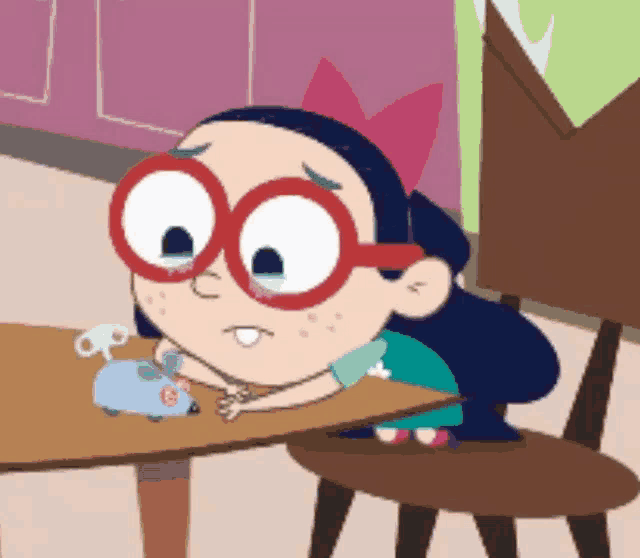 a cartoon girl wearing red glasses sits at a table with a toy mouse
