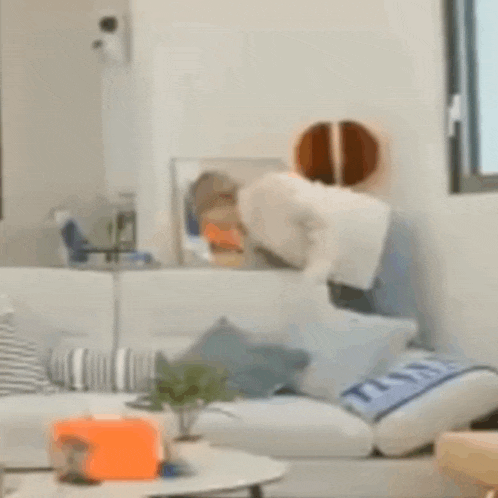 a person is standing on a couch in a living room with a basketball on the wall .