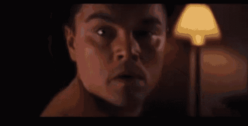 a man without a shirt is looking at the camera in a dark room .