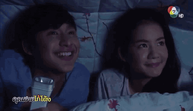 a man and a woman are laying in bed with a remote control in their hands .