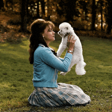 a woman is kneeling down holding a small white dog in her arms