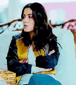 a woman is sitting on a couch with her arms crossed wearing a yellow and black jacket .