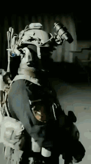 a man in a military uniform is standing in a dark room with a gun .