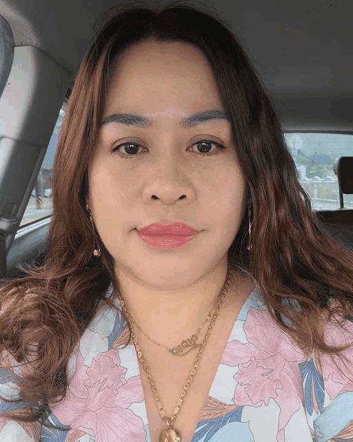 a woman in a car wearing a necklace that says ' aloha ' on it