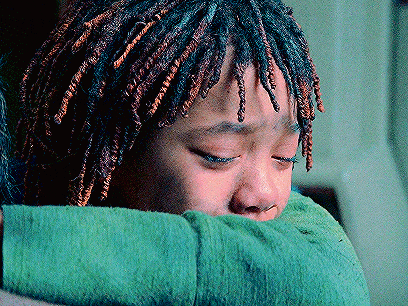 a young girl with dreadlocks is hugging a green sweater .