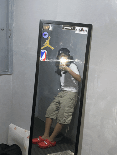 a person taking a selfie in front of a mirror with stickers on the wall including one that says red club