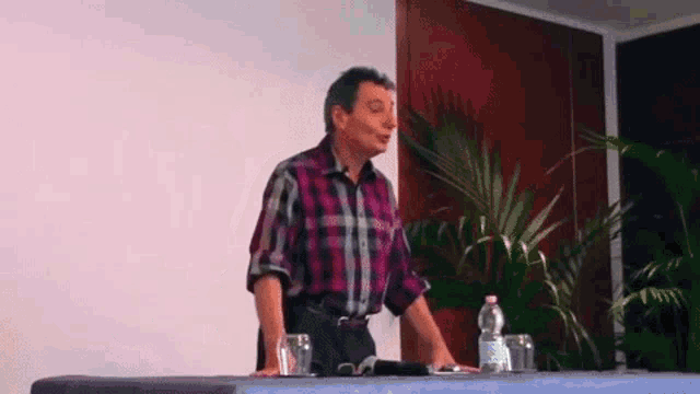 a man is standing at a table with a bottle of water and glasses .