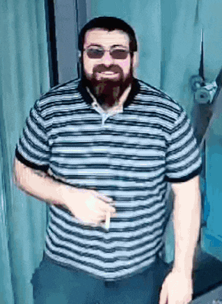 a man with a beard is wearing sunglasses and a striped shirt while smoking a cigarette .