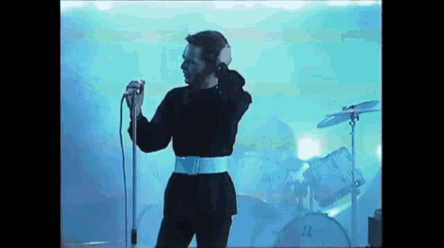 a man singing into a microphone in front of a drum set that says r on it