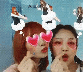 two girls wearing heart shaped sunglasses are making a heart with their fingers .
