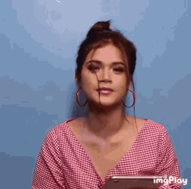 a woman wearing a plaid shirt and red hoop earrings is holding a tablet .