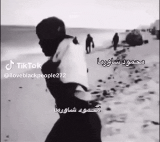 a black and white photo of a man standing on a beach holding a bag .