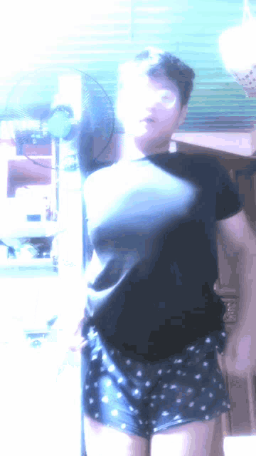 a person in a black shirt and shorts stands in front of a fan