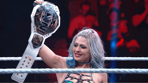 a woman in a wrestling ring is holding a championship belt that says nxt