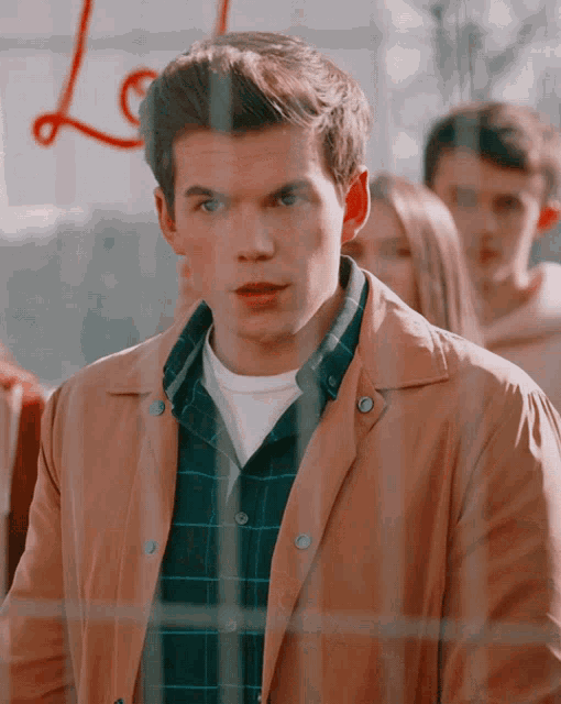 a man in a plaid shirt and a tan jacket stands in front of a sign that says " love "