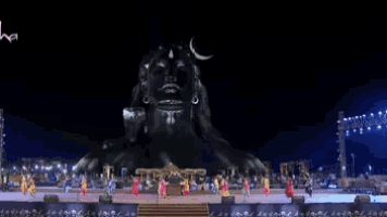 a group of people are dancing in front of a large statue