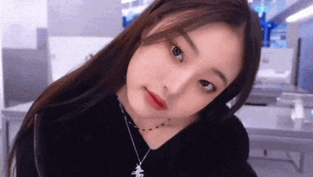a close up of a woman wearing a black shirt and a necklace looking at the camera