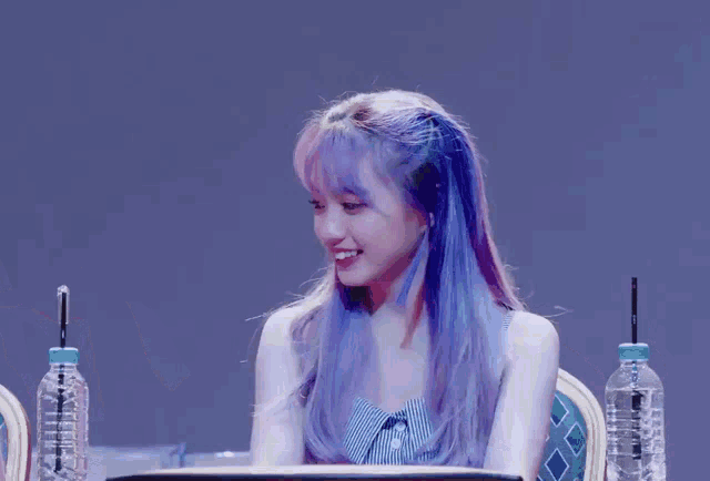 a girl with purple hair is sitting at a table with water bottles